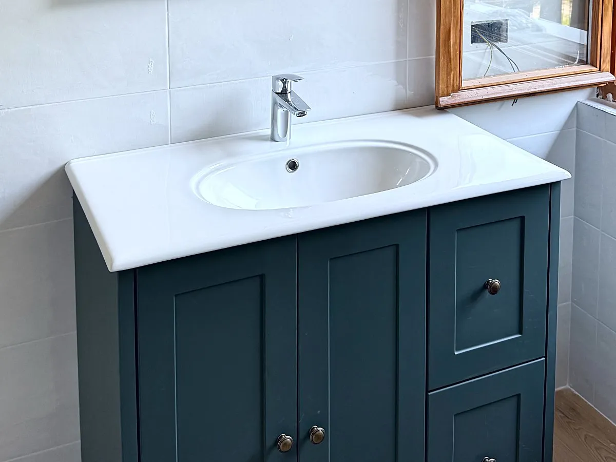 Bagno rifatto: lavabo bianco su mobile verde con ante a riquadri, accanto a una finestra in legno