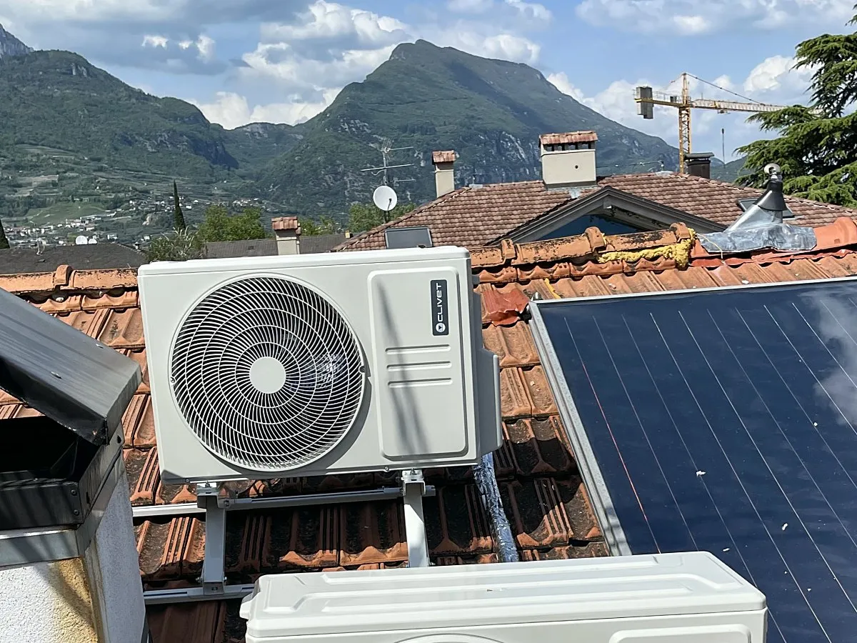 Unità esterne di due condizionatori sul tetto accanto a un pannello solare, con le montagne dell'Alto Garda dietro