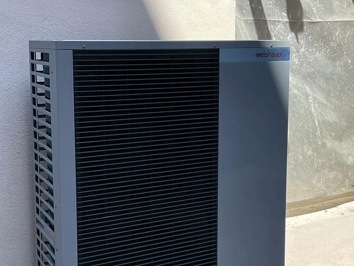 Unità esterna di una pompa di calore Weishaupt grigio antracite, appoggiata contro un muro bianco