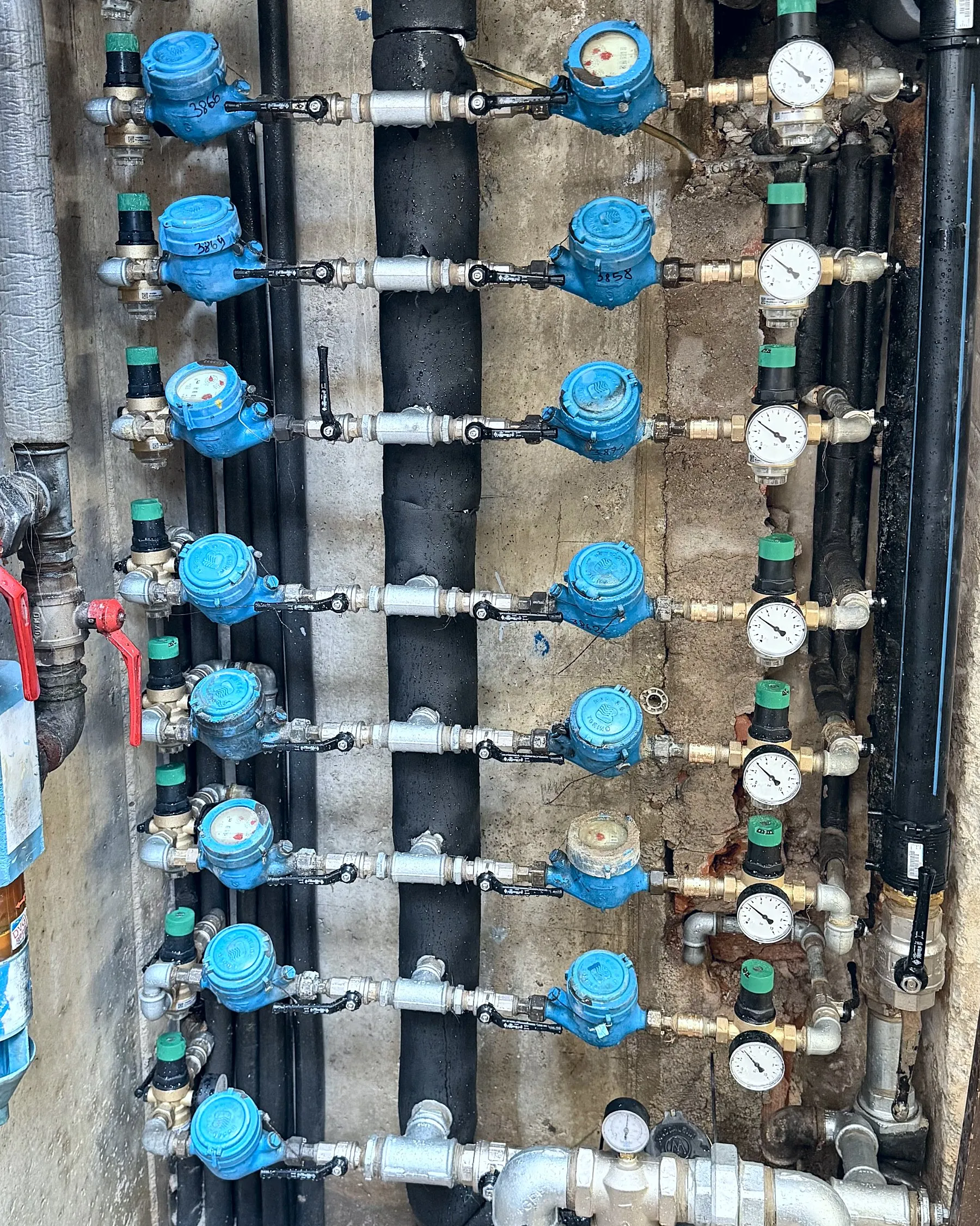Batteria di contatori dell'acqua con valvole, riduttori e manometri in un locale tecnico condominiale